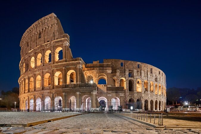 A night view of the Colosseum in Rome, Italy, illuminated against the dark sky.
