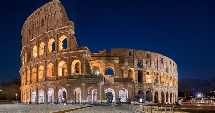 A night view of the Colosseum in Rome, Italy, illuminated against the dark sky.