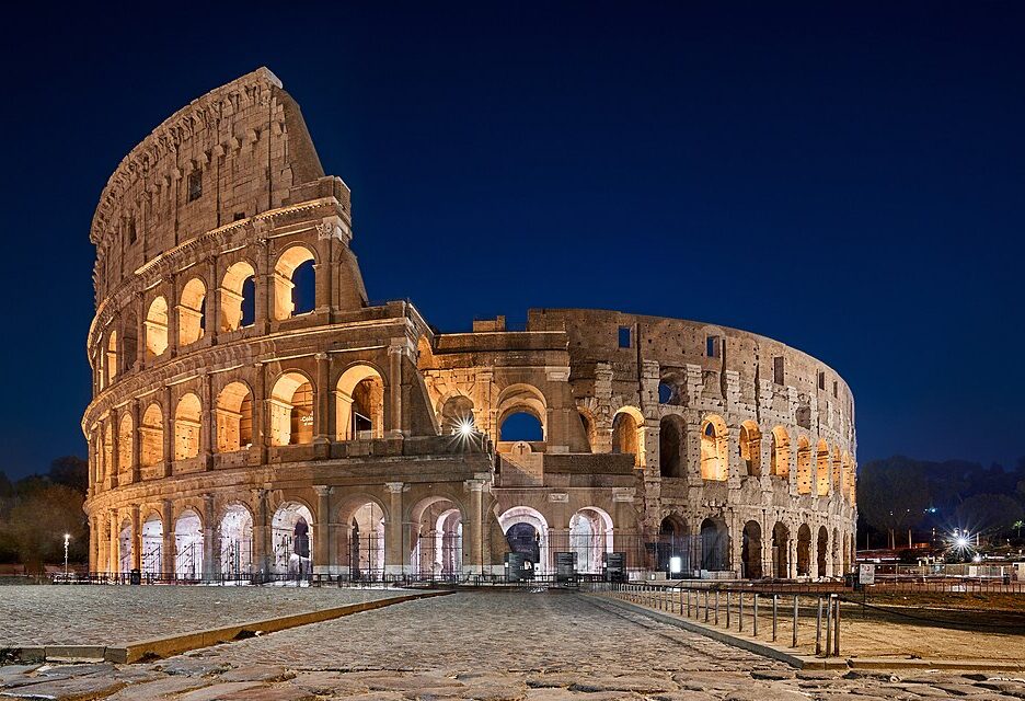 A night view of the Colosseum in Rome, Italy, illuminated against the dark sky.